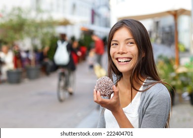 Woman Eating Traditional Danish Food Floedeboller Also Called Cream Buns Or Marshmallow Teacake. Girl Enjoying The Chocolate Covered Treat Outside In City Street Of Copenhagen, Denmark.