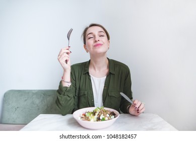 The woman eats a delicious salad. A sweet girl sits at the table, eats a plate salad and delights