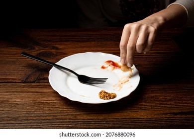 A Woman Eats Food From A White Plate In A Dark Room. Poverty, Last Meal Concept.