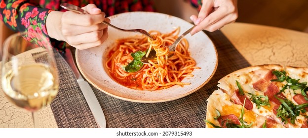 Woman eats Italian pasta with tomato, meat. Close-up spaghetti Bolognese wind it around a fork with a spoon. Parmesan cheese