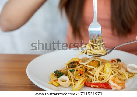 Woman eats Italian spicy seafood pasta . Close-up  spicy seafood spaghetti wind it around a fork with a spoon. 
