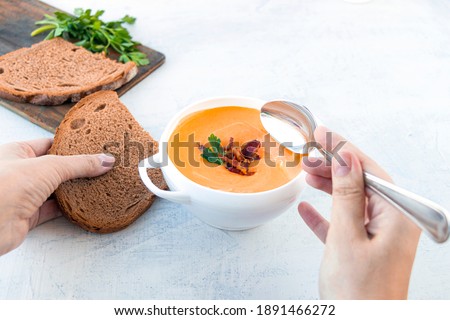 A woman eats pumpkin soup with fried bacon with bread. Pumpkin cream soup in a white plate on a napkin on a white background. Top view. Copy space