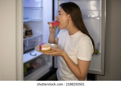 Woman eats a sweet delicious calorie sandwich with cream in her pajamas at night near the refrigerator. Concept: night meal, calories, food during stress and depression, bulimia, eating disorder - Shutterstock ID 2188250501