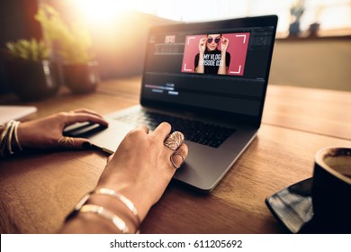 Woman editing video on laptop computer for her vlog. Woman wearing fashionable rings working on laptop on a wooden table.