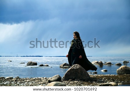 woman in Elvish cloak walks along the shore to the sea