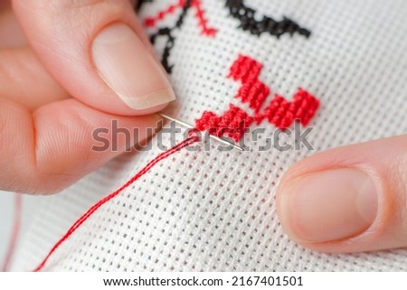 A woman embroiders the national symbols of Ukraine with a cross. Close-up of female hands cross-stitching on white canvas.