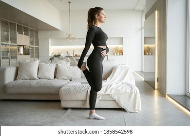 A woman is engaged in aerobics with her health doing stretching and cardio exercises. Large bright apartment. workout fitness gym at home in the living room, comfortable sportswear in black.