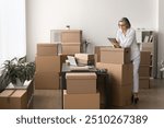 Woman engaged in managing orders and inventory for e-commerce or small business, working in stockroom using tablet, check, update order information. Labeling, packaging, dispatching parcels workflow