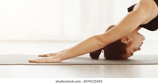 A woman is engaged in a yoga session, executing the Downward Facing Dog pose with precision and focus. Her hands are firmly planted on a yoga mat, closeup, panorama with copy space - Powered by Shutterstock