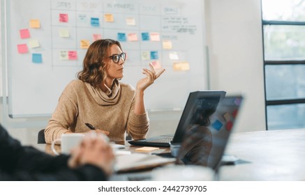 Woman engaging in a collaborative brainstorming session with her colleagues in a boardroom. Business people discuss ideas and manage projects. They work together on software development. - Powered by Shutterstock