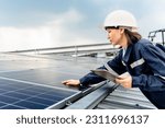 Woman engineer electrician using a hand to check solar panels on the roof, clean energy power nature, photovoltaic systems, the energy produced by the sun, sustainable business concept. 