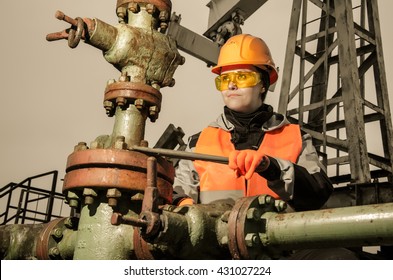 Woman engineer in the oil field repairing wellhead with the wrench wearing orange helmet and work clothes. Oil and gas concept. Toned.