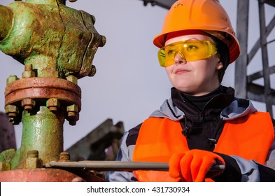 Woman engineer in the oil field repairing wellhead with the wrench wearing orange helmet and work clothes. Oil and gas concept. 