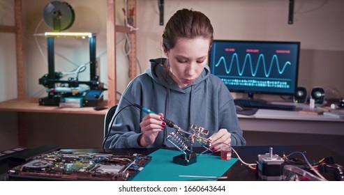 A woman engineer solders circuits sitting at a table. Microchip production factory. Technological process. Assembling the PCB board. Girl repairing electronic device on the circuit board. - Powered by Shutterstock