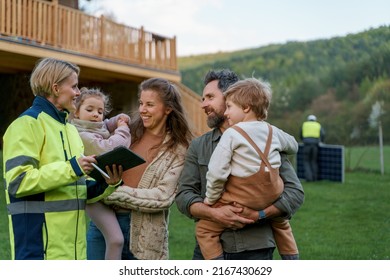 Woman Engineer Talking To Young Family About Solar Panel Installation In Front Of Their House.