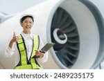 Woman engineer in white hardhat standing and holding tablet working aircraft maintenance mechanics moving through hangar.