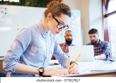 Woman Engineer Working On Blueprint In Office With Colleagues On Background