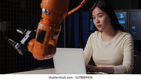 Woman Engineers With Laptop Analyse Control Robotic Arm Works And Moves. She Are In A High Tech Research Laboratory With Modern Equipment. Technology And Innovation Concept.