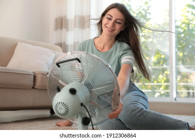 Woman enjoying air flow from fan on floor in living room. Summer heat