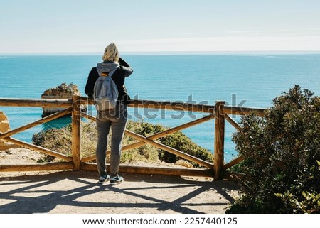 A woman enjoying the Atlantic Ocean from the top of cliffs at Marinha Beach in Algarve, Portugal