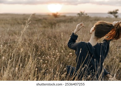 Woman enjoying the breeze in a sunlit field with her hair dancing in the wind during sunset - Powered by Shutterstock