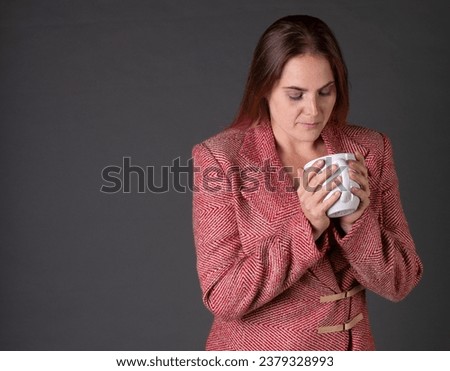 A woman enjoying a cup of coffee in a tacky business suit on a grey background