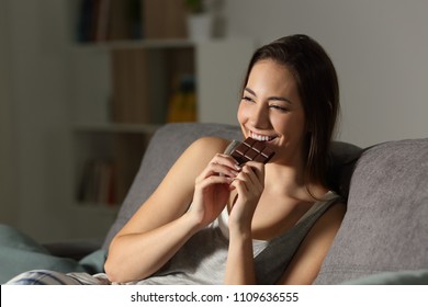 Woman enjoying eating chocolate in the night sitting on a couch in the living room at home - Powered by Shutterstock