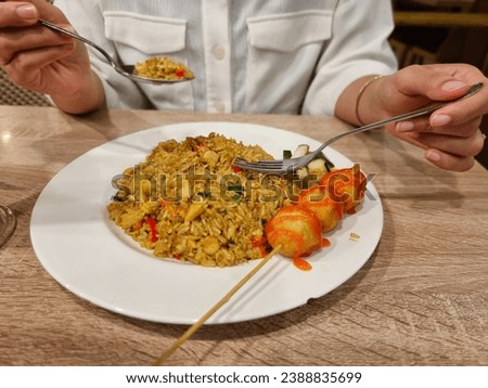 A woman is enjoying fried rice and shrimp meatballs at a restaurant. Eat fried rice using a spoon and fork. Asian food cuisine.