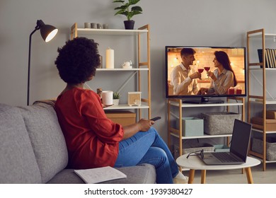 Woman Enjoying Good Romcom Serial In The Evening. Single African American Lady Sitting Alone At Home, Drinking Coffee And Watching Romantic Love Story On Soap Opera Entertainment TV Channel, Back View