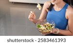 Woman enjoying a healthy salad while sitting at home in athletic wear.