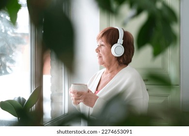 woman enjoying her cup of tea or coffee while listening to music feelings of comfort and relaxation. elderly people who seek comfort and relaxation in their daily lives. - Shutterstock ID 2274653091