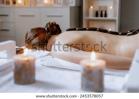 Woman enjoying hot stone massage at spa salon. Professional masseur making stone therapy. Relaxing and ease tense muscles and damaged soft tissues throughout body.