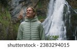 Woman enjoying a mighty waterfall in forest at rainy day. Girl takes a deep breath of fresh air in autumn nature. Gollinger Wasserfall.