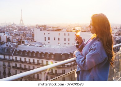 Woman Enjoying Panoramic View Of Paris And Eiffel Tower At Sunset, Holding Glass Of Wine Or Champagne In Rooftop Luxury Restaurant