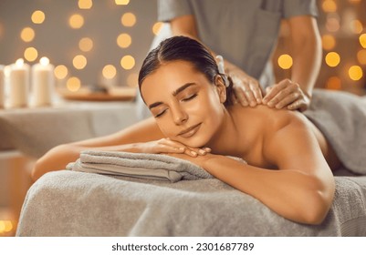 Woman enjoying professional body massage at a modern spa salon. Relaxed young lady lying on a massage table while a skillful masseuse is gently massaging her back. Beauty, health, pleasure, concept - Shutterstock ID 2301687789