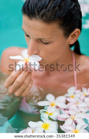 woman enjoying pure waters with beautiful plumeria flowers smelling fragrant aroma in tropical spa