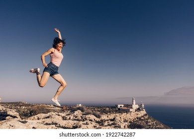 Woman Enjoying Trip With Rv Motor Home, Jumping In The Air At Camper. Mesa Roldan Lighthouse Location, Almeria Spain. Happiness And Traveling.