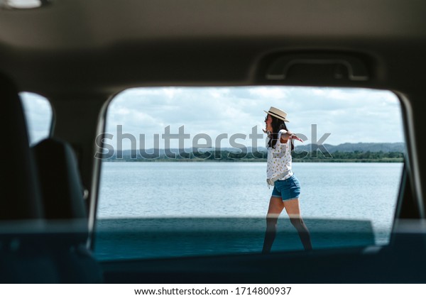 woman enjoying vacation through\
a window of a luxury van, woman in shorts and white blouse with\
hat