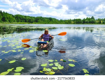 woman enjoying weekend rowing on transparent boat in small lake, bright sunlight, cloud reflections, sunny summer day