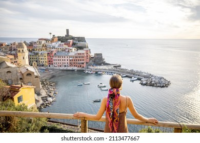 Woman enjoys beautiful landscape of coastline with old Vernazza village, traveling famous Cinque Terre towns in northwestern Italy. Summer vacation on the Mediterranean coast concept