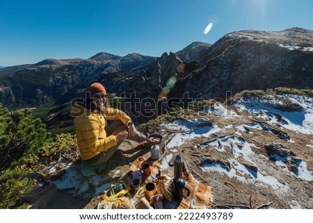 A woman enjoys a beautiful view of rocks and mountains while having a picnic with a tourist equip