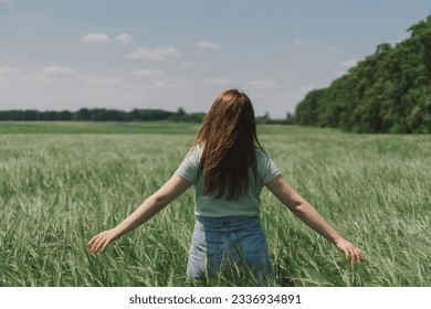 A woman enjoys the fresh air in nature in a green barley field. Summer countryside and gathering flowers. Atmospheric tranquil moment. Back view. - Shutterstock ID 2336934891