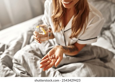 A woman enjoys her morning in bed, sipping water and taking her medication, embodying selfcare and wellness. This scene illustrates positive morning routines for health and happiness - Powered by Shutterstock