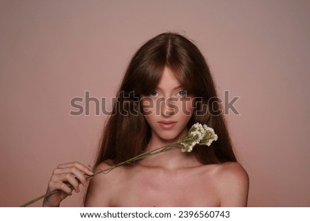 A woman enjoys her skin touching her face with wildflowers. Seminude longhaired woman in studio on brown background close up. The concept of beauty, cosmetology and care.