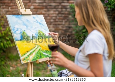 Woman enjoys  painting on canvas and drinking wine outdoor.