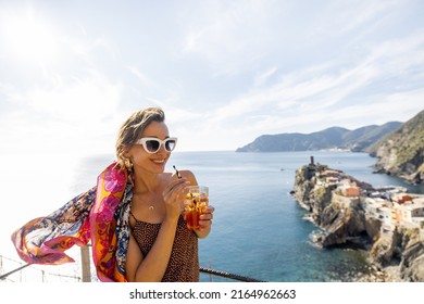 Woman enjoys summer cocktail and beautiful landscape of mediterranean coast in Vernazza village. Traveling famous Cinque Terre towns in northwestern Italy. Idea of summer vacation - Shutterstock ID 2164962663
