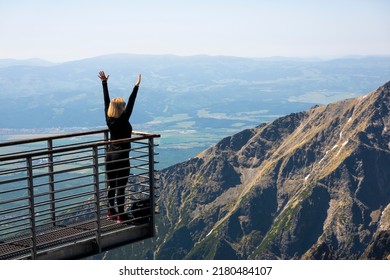 A woman enjoys the view and joy on the iron structure on the Lomnick peak of the High Tatras, Slovakia