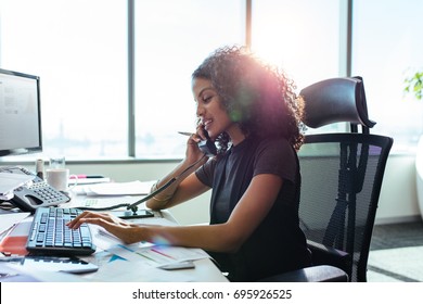 Woman entrepreneur busy with her work in office. Young woman talking over telephone while working on computer at her desk.