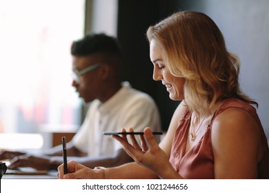 Woman entrepreneur writing in notepad while talking over mobile phone. Man working on laptop sitting at a coffee shop. - Shutterstock ID 1021244656