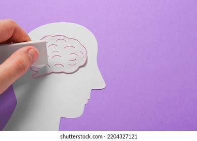 Woman Erasing Brain On Human Head Paper Cutout On Violet Background, Top View With Space For Text. Dementia Concept